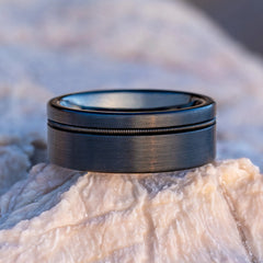 Solus black tungsten ring with guitar string on a rock by Natural Rings